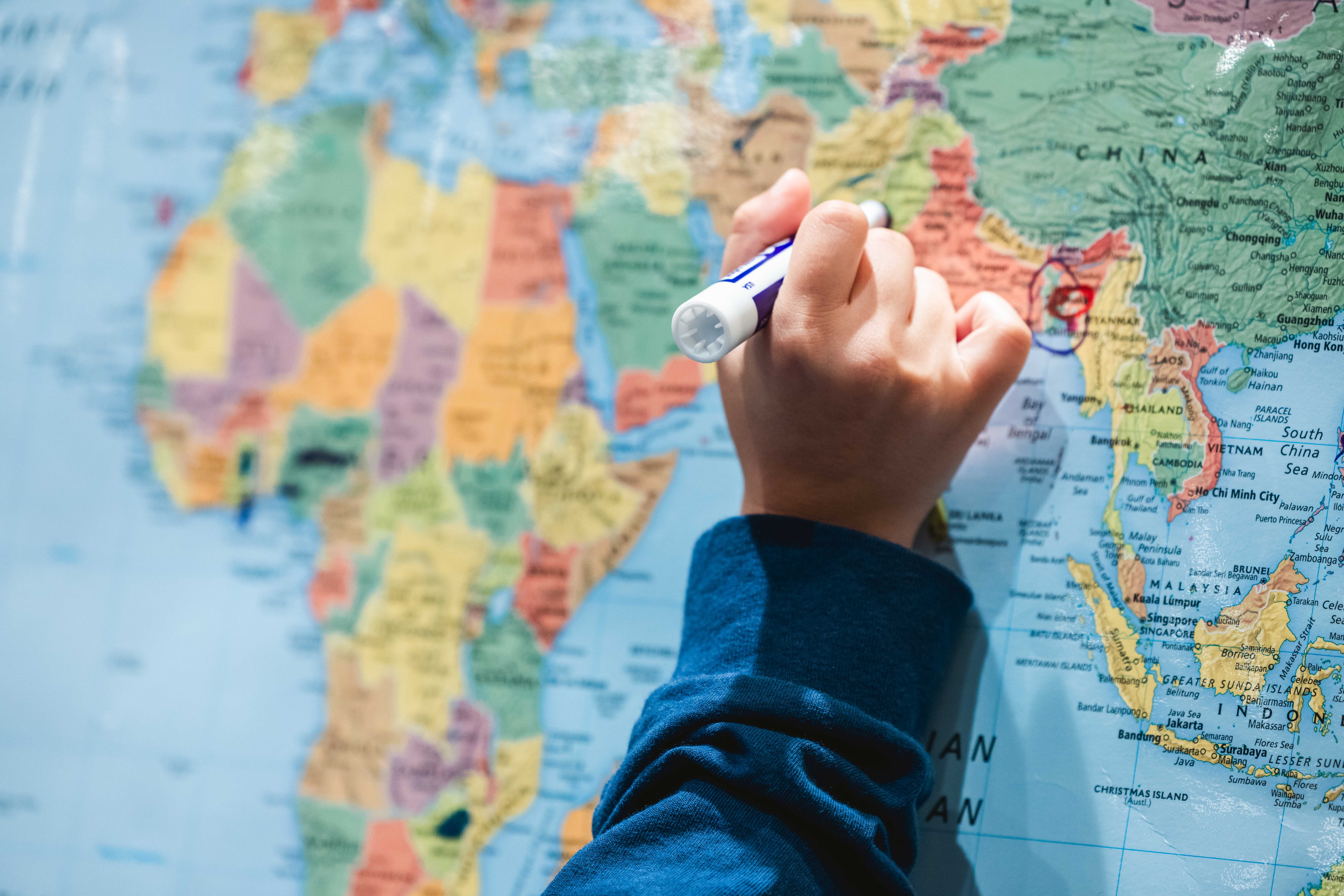 hand with marker pointing at poster of world map